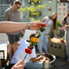 Person hält Gemüse-Grillspieß bei sonniger Grillparty auf Terrasse