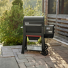Weber SEARWOOD Holzpelletgrill in Schwarz auf einer Terrasse mit grüner Umgebung