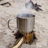 Petromax Kochbecher auf Sand mit brennendem Holz und Rauch
