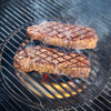 Steaks auf einem Holzkohlegrill mit sichtbarem Diffusorring und glühenden Kohlen