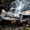 Gusseisen Stapelrost mit Speck und Eiern über offenem Feuer im Wald