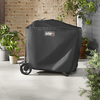 Schwarze Weber Traveler Premium Abdeckhaube über einem Grill neben Pflanzen