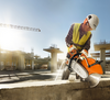 Bauarbeiter verwendet STIHL Trennschleifer auf Baustelle mit Betonstrukturen und Kran im Hintergrund