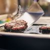 Rinderhacksteaks auf einem Elektrogrill mit sichtbarem Dampf und einem Spatel