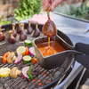 Hand taucht Hühnerflügel in Sauce auf einem mit Gemüse belegten Holzkohlegrill