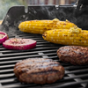 Maiskolben und Burger auf einem Gasgrill mit aufsteigendem Rauch