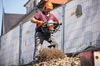 Mann verwendet STIHL BT 131 Erdbohrgerät auf Baustelle mit Sicherheitsausrüstung und Cartoon-Plane im Hintergrund