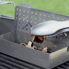 Hand fügt mit Grillzange Holzchips in Weber Räucherbox auf Grillrost