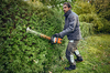 Mann in Schutzhose schneidet Hecke mit motorisierter Heckenschere