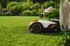 STIHL iMOW 7 Mähroboter auf Rasen im Garten neben Ladeplatte