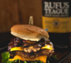 Burger mit Käse und Rufus Teague BBQ Sauce auf Holztisch