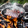 Petromax Gusseisenpfanne auf offenem Feuer mit Fleisch und Tomaten