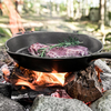 Gusseisenpfanne mit Fleisch über offenem Feuer im Wald