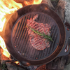 Petromax Gusseisen-Grillpfanne über offenem Feuer mit gebratenem Steak und Rosmarin