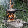 Petromax Feuerpfanne auf tragbarem Holzfeuerofen in natürlicher Umgebung beim Kochen