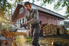 Mann benutzt STIHL Kettensäge zum Schneiden eines Holzstamms vor einem roten Holzhaus