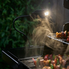 Weber WORKS flexible Lampe beleuchtet Grillrost bei Nacht mit gegrillten Speisen auf Spießen