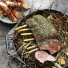 Gegrilltes Lammrack mit Kräutern auf Heubett neben Speck umwickelten Birnen