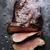 Gegrillter Rinderbraten in Scheiben auf dunklem Untergrund mit Rauch und Salz