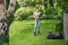 Frau bedient STIHL iMOW 5 EVO Mähroboter mit Tablet in einem blühenden Garten