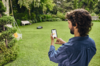 Mann bedient Smartphone im Garten während Mähroboter Rasen mäht
