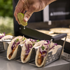 Hand drückt Limettensaft über gefüllte Tacos im Weber Taco Rack neben einem Grill