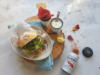 Sandwich mit Hähnchen und Rucola, rote Chips, weiße Sauce und Gewürzdose auf Marmortisch