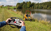 Person bedient ferngesteuerten Aufsitzmäher AS 940 Sherpa 4WD RC an einem sonnigen Tag neben einem Teich