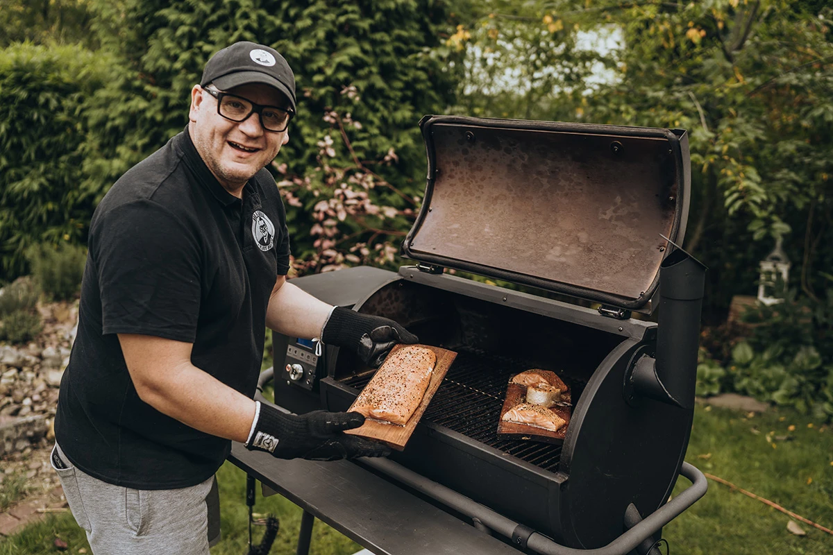 Mann bereitet Lachs auf Grill zu, umgeben von grünem Garten
