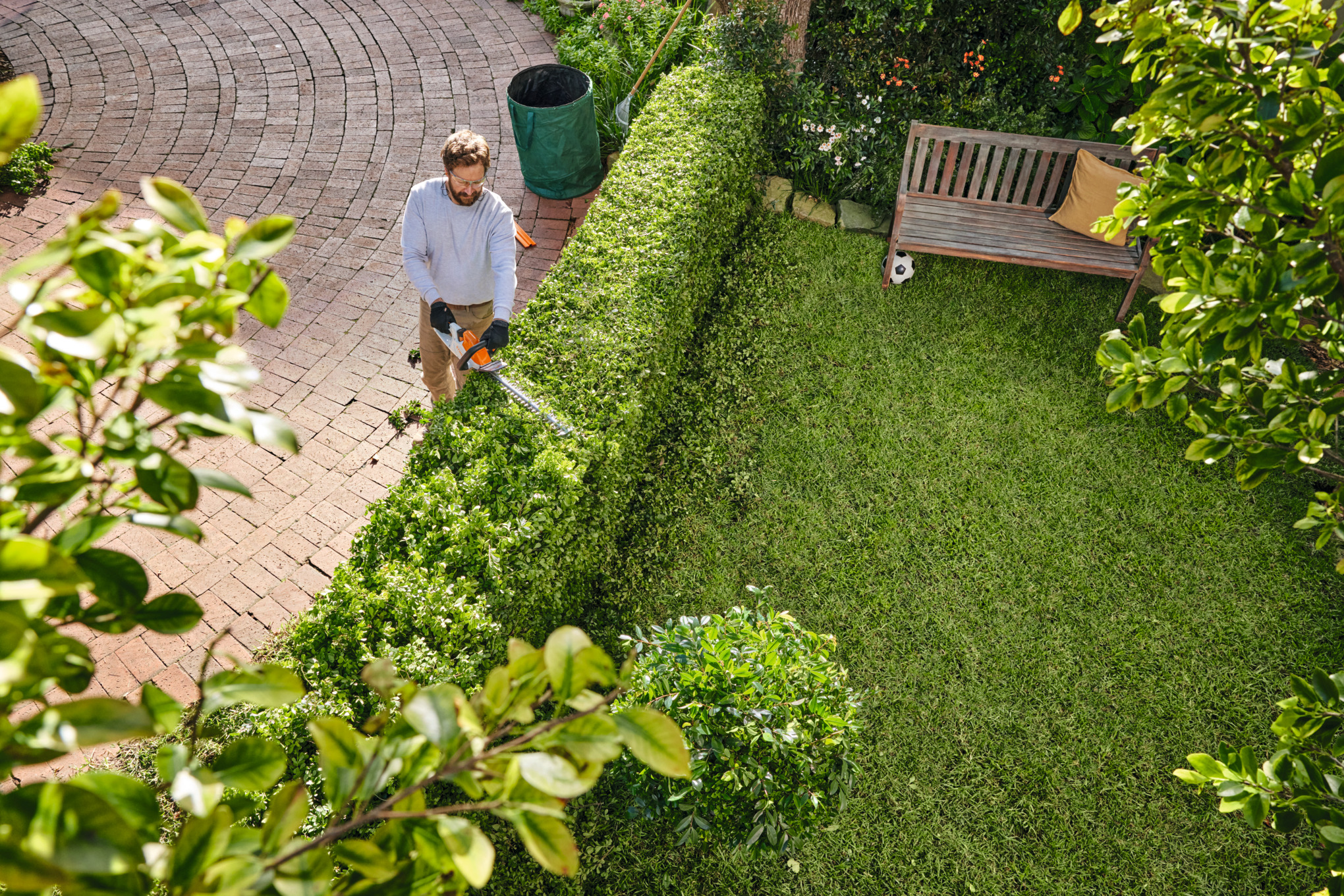 Mann verwendet STIHL Akku-Heckenschere HSA 40 in einem sonnigen Garten
