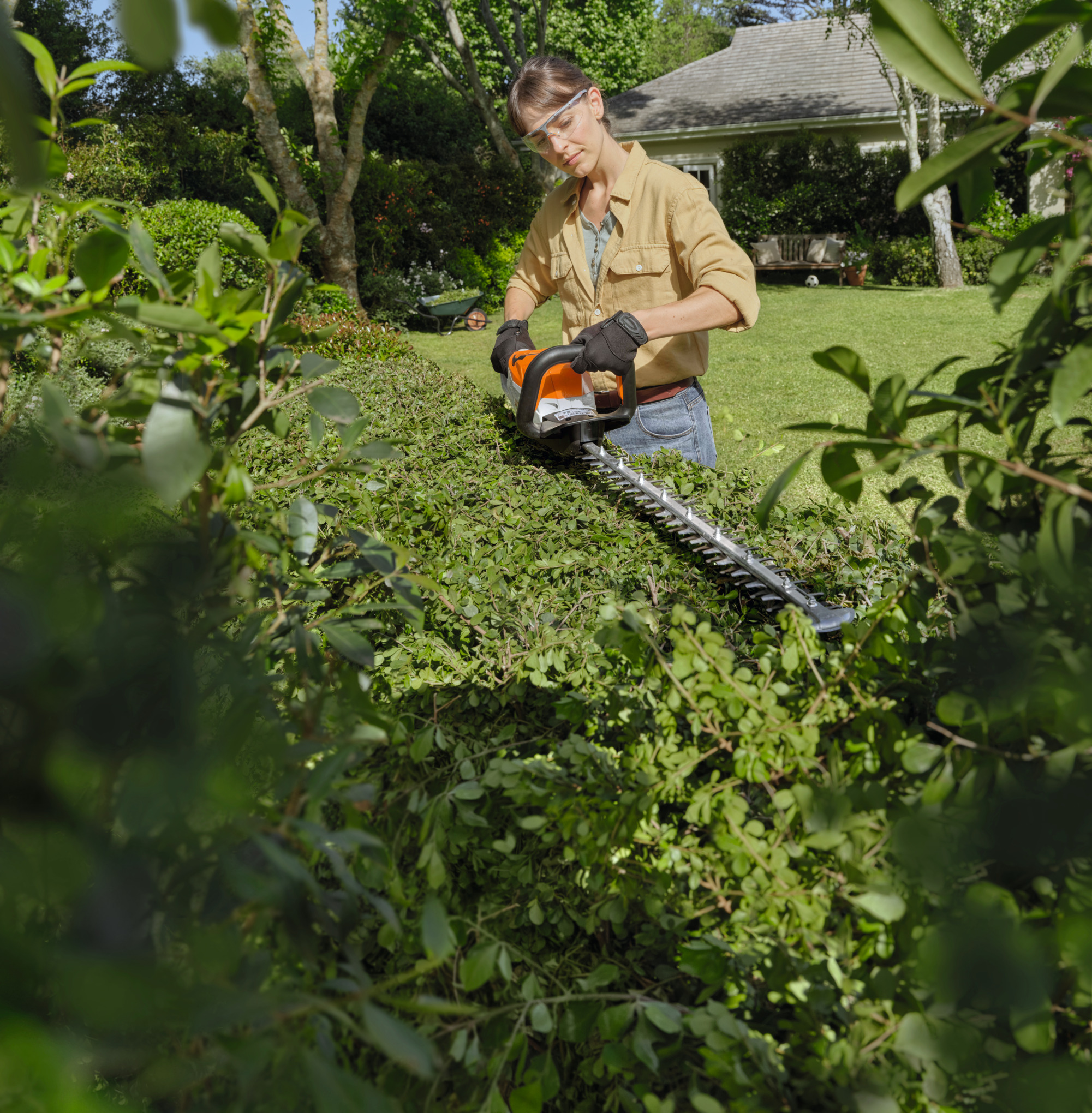 Frau benutzt STIHL HSA 60 Akku-Heckenschere in einem sonnigen Garten
