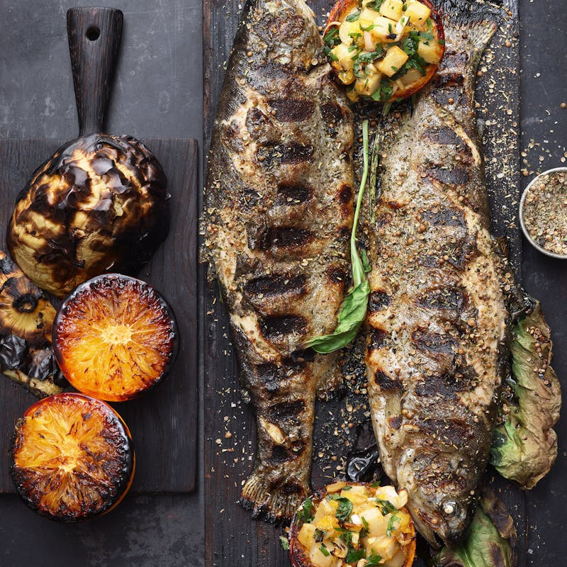Gegrillte Fische und Gemüse auf dunklem Holzbrett