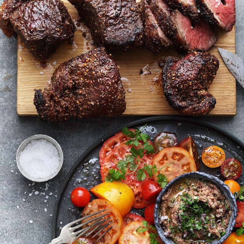 Gegrillte Steaks und frische Beilagen auf Holzbrett und schwarzem Teller