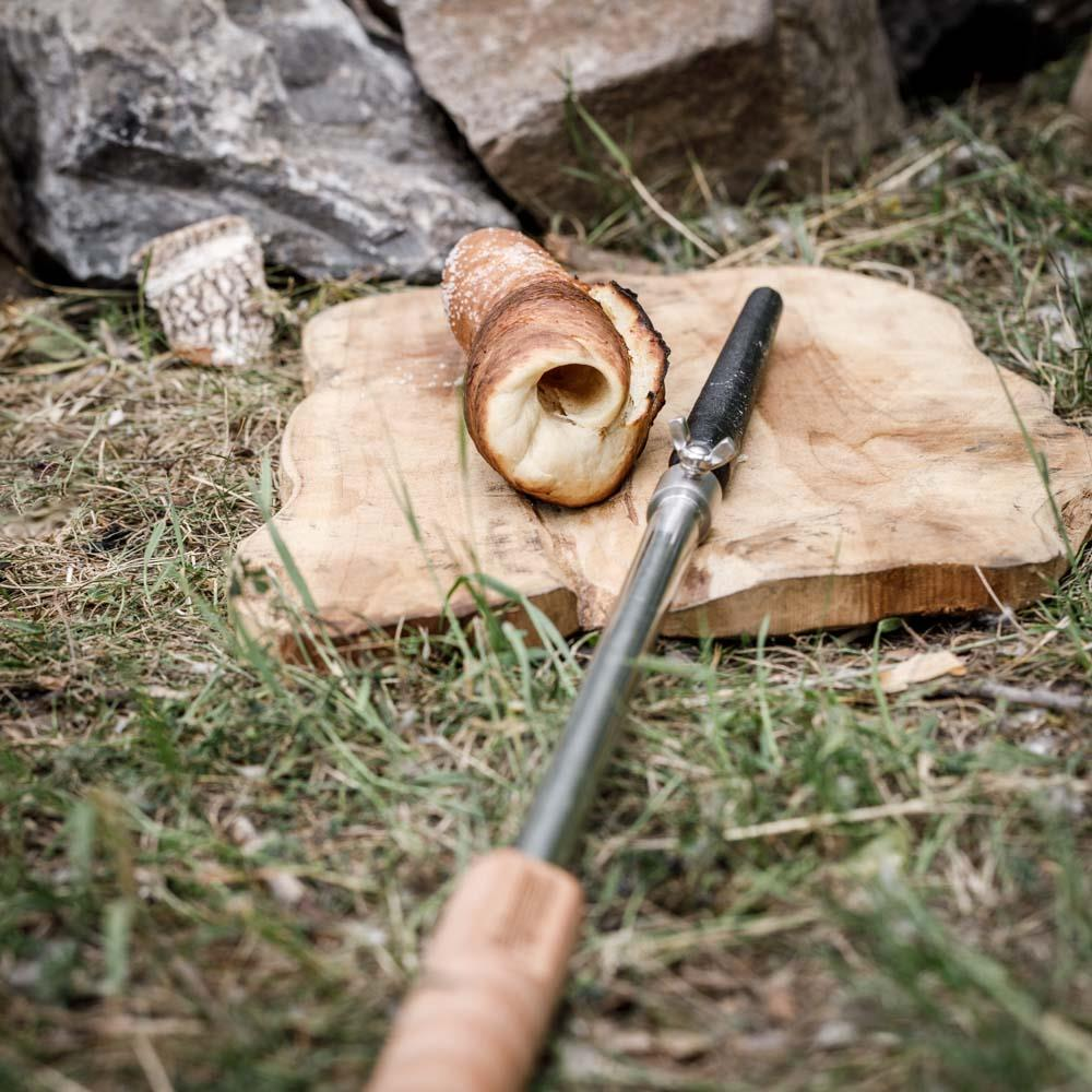 Petromax Stockbrot Spieß mit Gusseisenspitze und gebackenem Brot auf einem Holzbrett im Freien