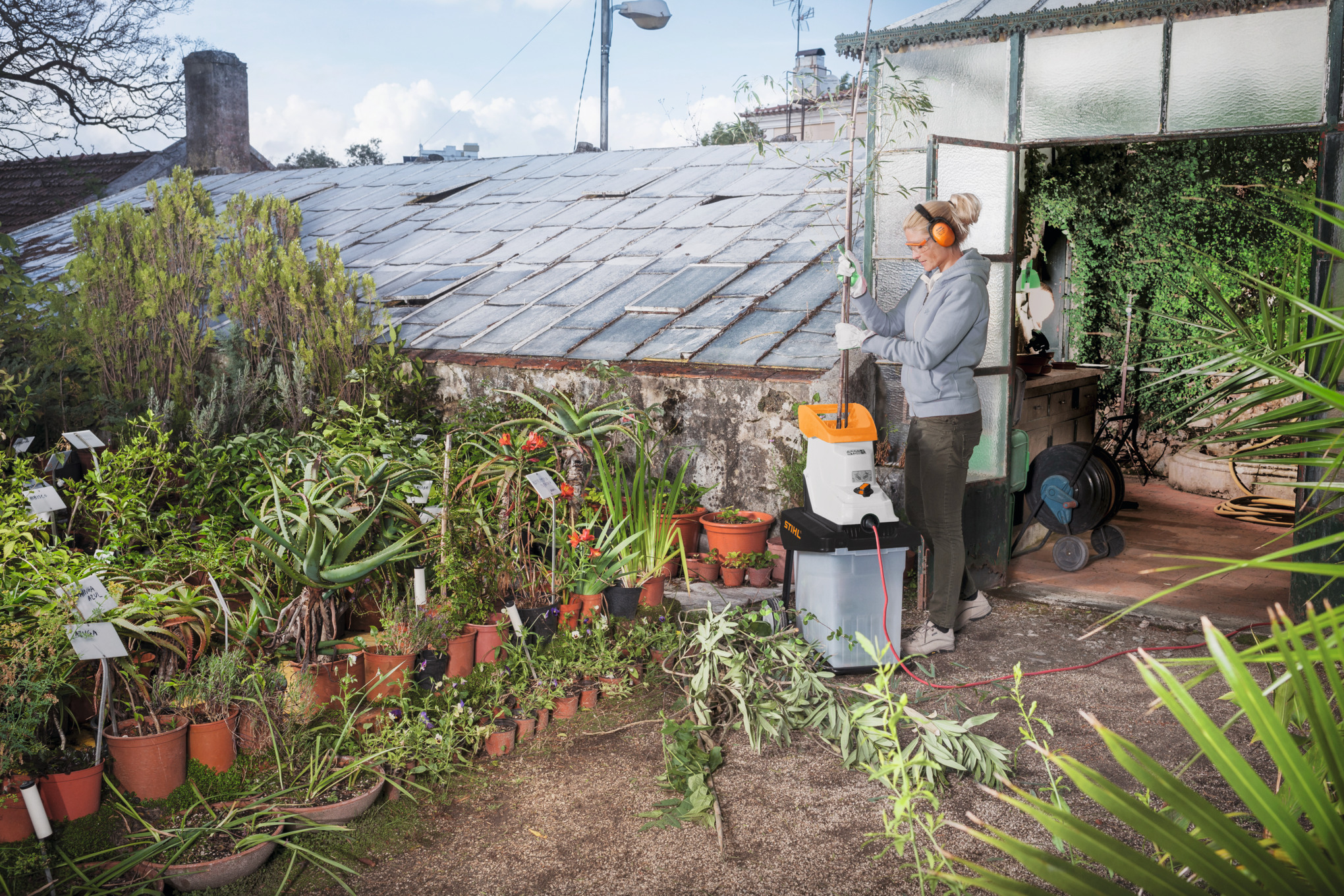 Ältere Frau verwendet STIHL GHE 135 L Häcksler in einem üppigen Garten