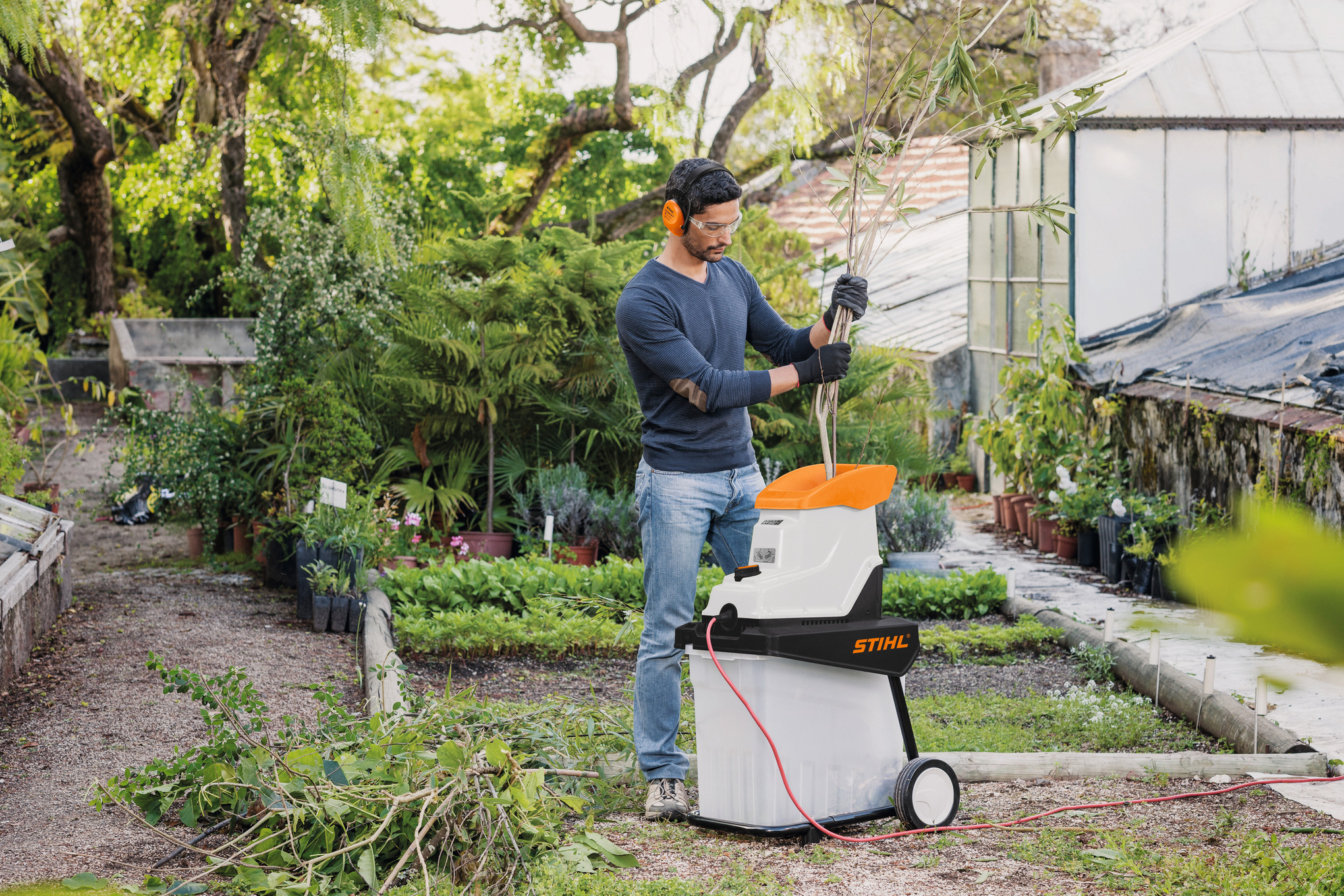 Mann verwendet STIHL GHE 135 L Gartenhäcksler in einem grünen Garten
