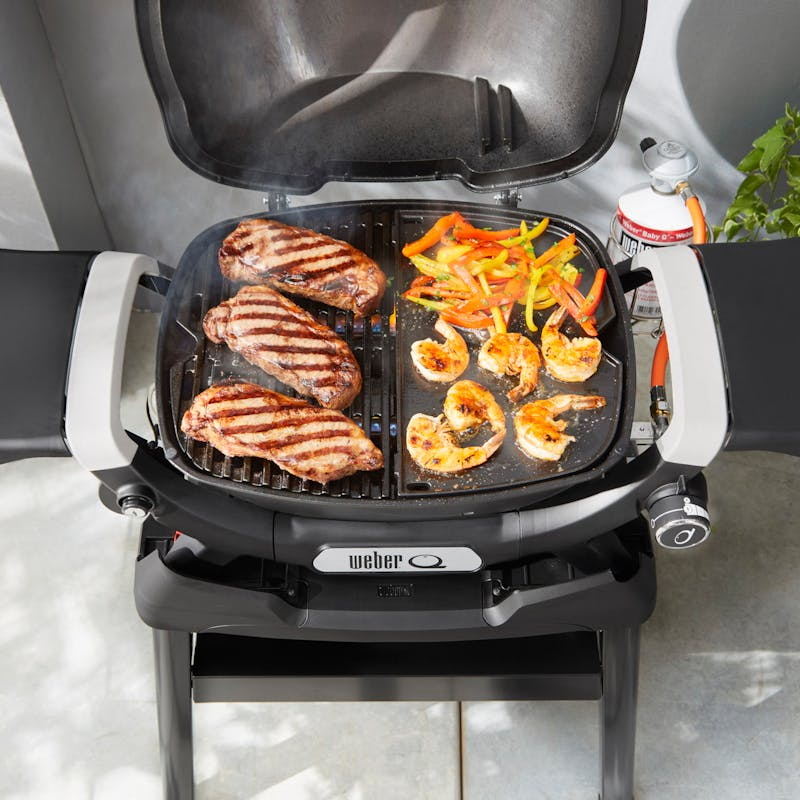 Weber Q Gasgrill mit Steaks und Garnelen auf Grillplatte im Freien