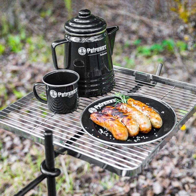 Petromax Perkolator und Tasse auf Grillrost mit gegrillten Würstchen im Freien