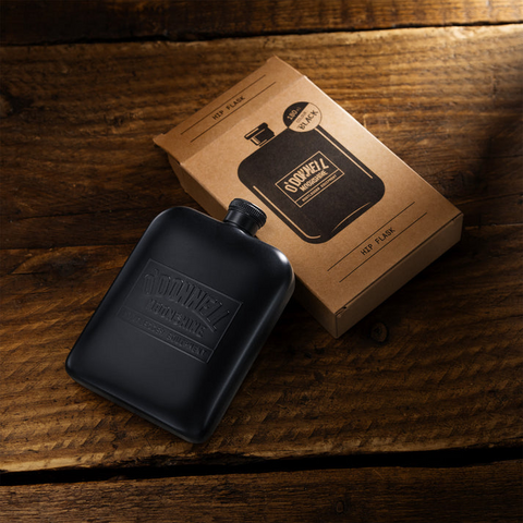 Mattschwarzer O'Donnell Moonshine Flachmann neben Kartonverpackung auf Holztisch
