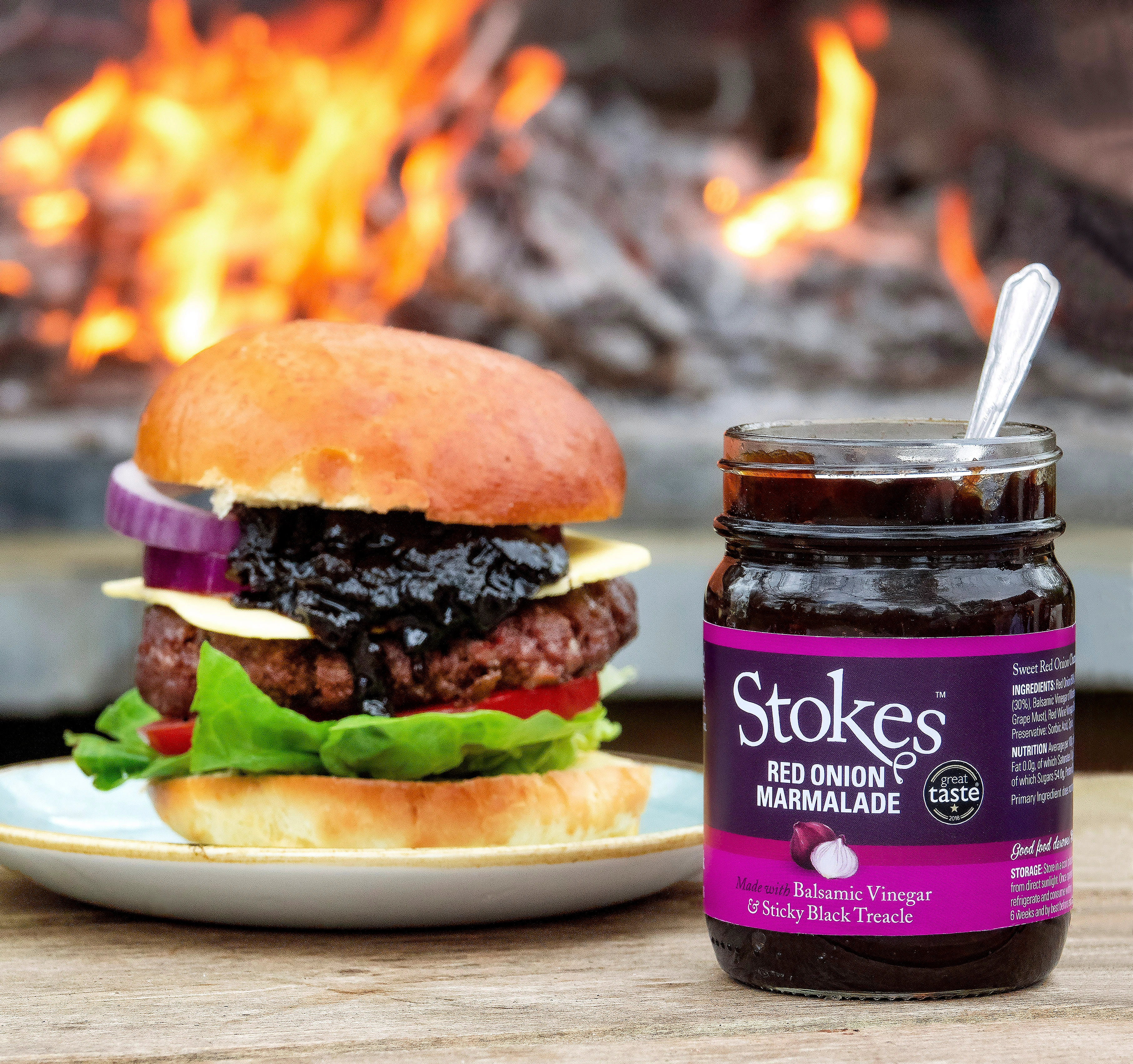 Stokes Red Onion Marmelade im Glas vor einem Burger und offenem Feuer