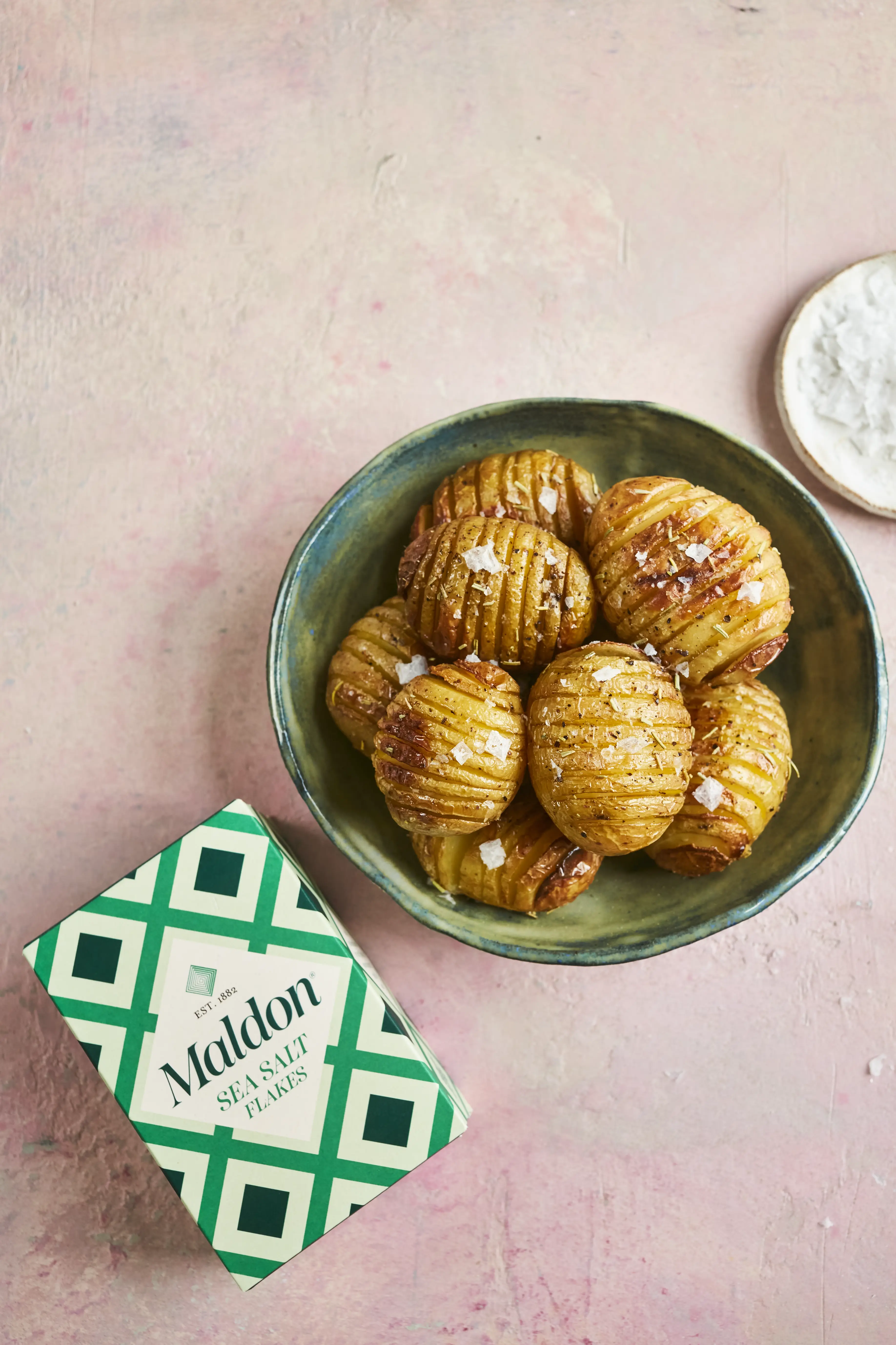 Hasselback potatoes seasoned with sea salt in a bowl beside Maldon Sea Salt Flakes box