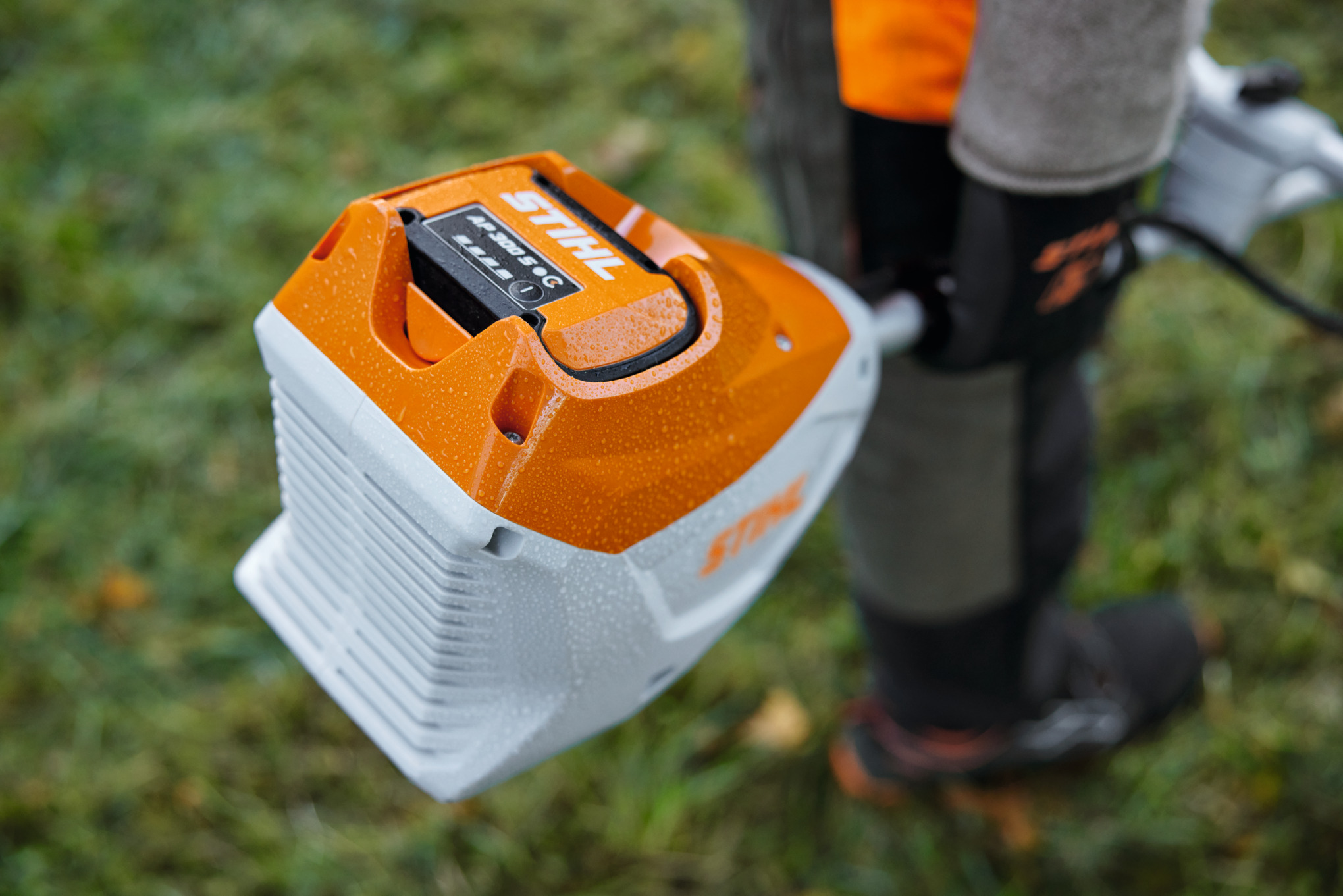Nahaufnahme eines STIHL FSA 120 Akkupacks an einer Motorsense getragen von einer Person in Arbeitskleidung