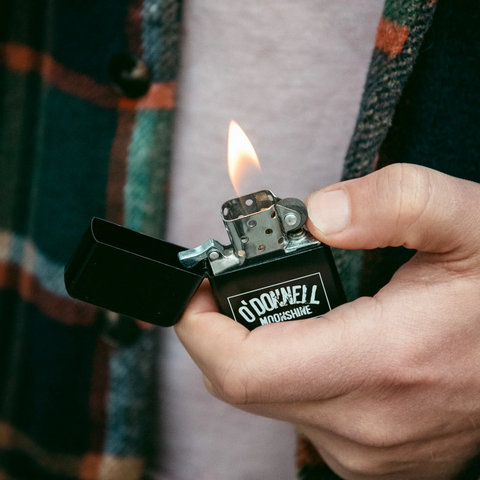 Hand hält geöffnetes O'Donnell Moonshine Benzinfeuerzeug mit sichtbarer Flamme