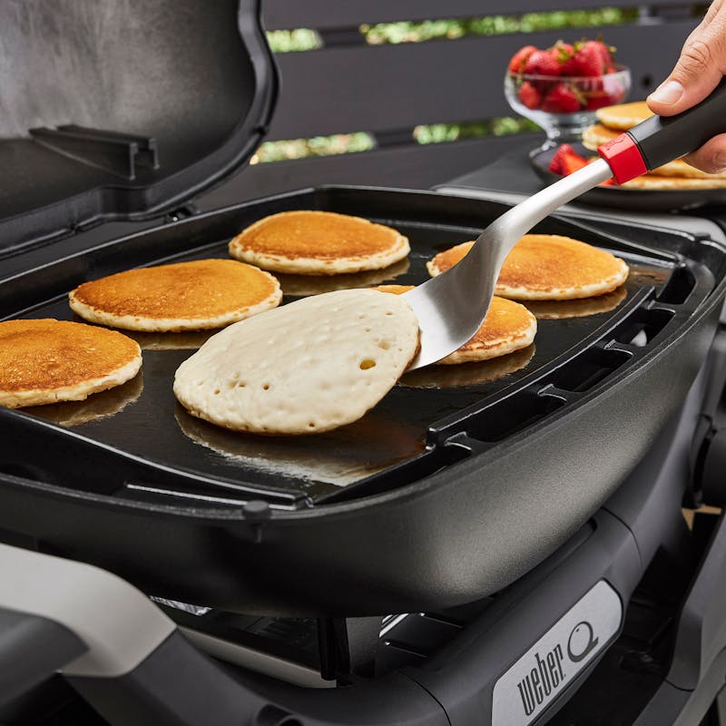 Person wendet Pfannkuchen auf Weber Q3000N Grillplatte im Garten