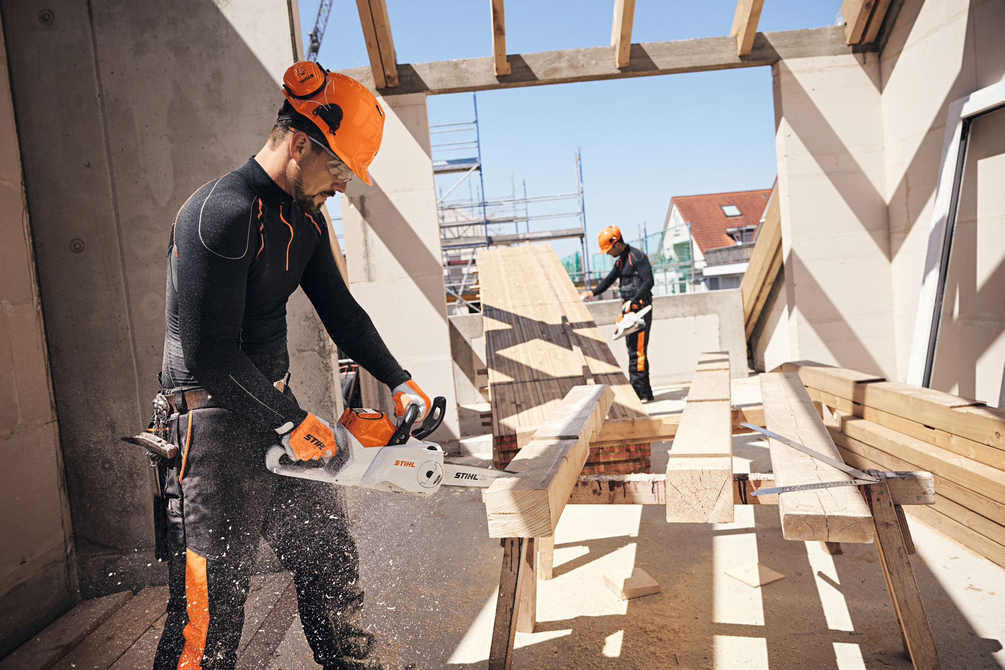 Zwei Männer mit Schutzausrüstung arbeiten mit STIHL Akku-Kettensägen auf Baustelle