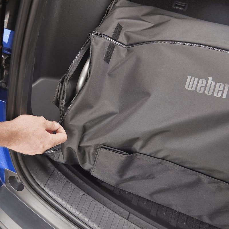 Mann schließt Reißverschluss eines Weber Traveler Kofferraumschutzes im Auto