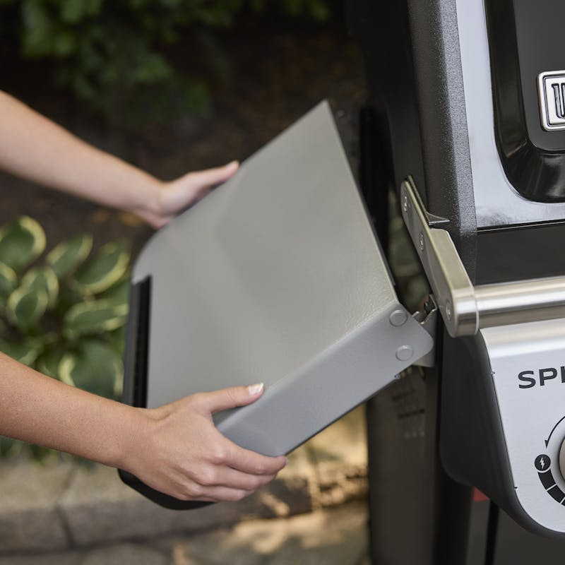 Person befestigt Seitentisch an Weber SPIRIT E-325 GBS Gasgrill im Garten