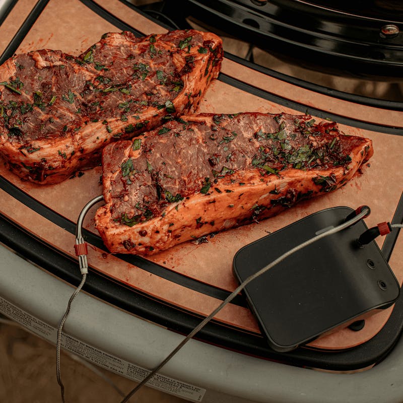 Gewürzte Fleischstücke auf Weber Traveler Schneidebrett neben Grill