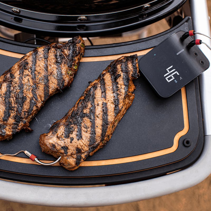 Zwei gegrillte Steaks auf Weber Traveler Schneidebrett neben einem Grillthermometer