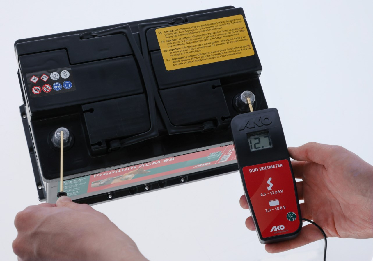 Hand hält AKO DUO-Voltmeter zur Spannungsprüfung an einer Batterie